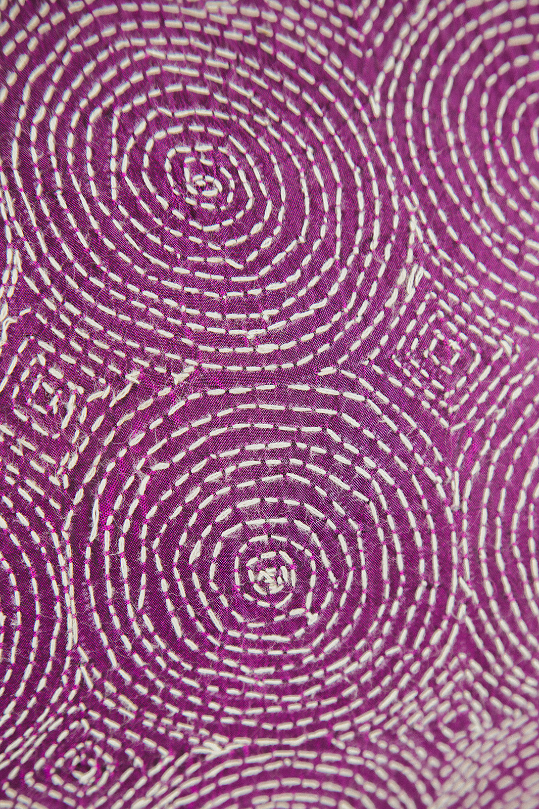 A close-up of a purple cushion textile with an allover white circular and dotted geometric pattern.