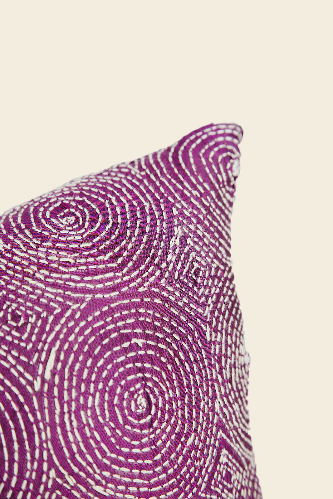 A close-up of a decorative throw pillow featuring a vibrant magenta-purple and white circular spiral pattern, shown against a solid light beige background.